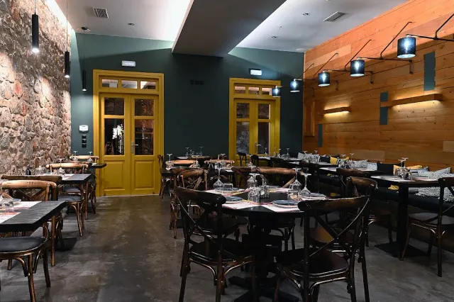 A dining room with a stone wall, yellow doors and dark wooden chairs around the tables