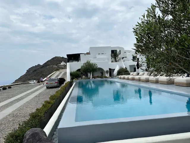 A long pool with sun loungers, and a white building on a rocky slope behind it