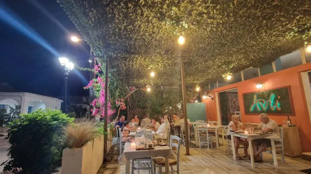 Diners in the evening under a canopy of foliage with hanging bulbs and a lit orange wall