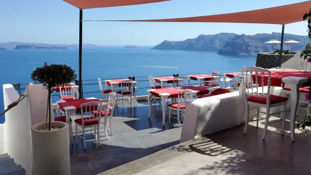 A terrace with orange shade sails, white chairs and red cushions facing the sea