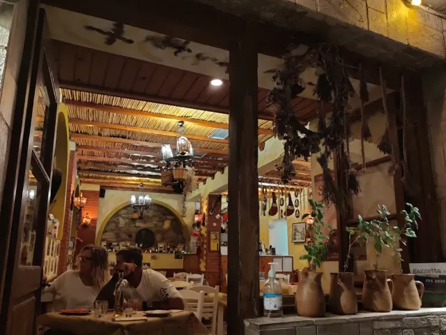 A lit interior with a reed ceiling, hanging herb bundles and clay jugs on a ledge