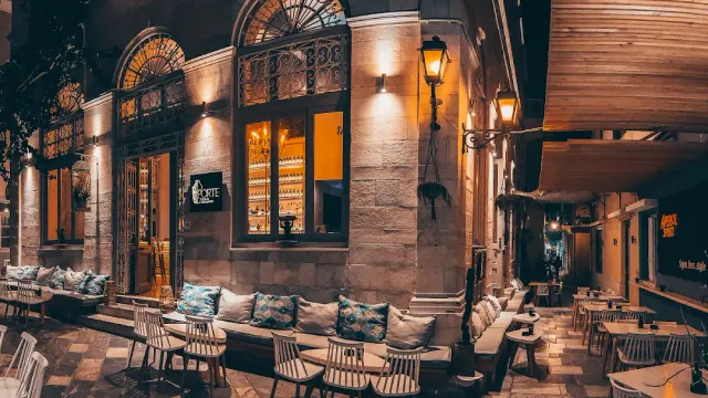 A stone building corner at night with arched windows, cushioned benches and street lamps