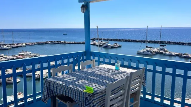 A checked cloth table on a blue balcony, facing a jetty and moored boats