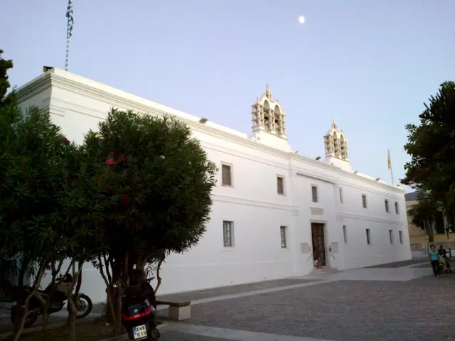 A long white church complex with crosses on the roof and trees in the courtyard