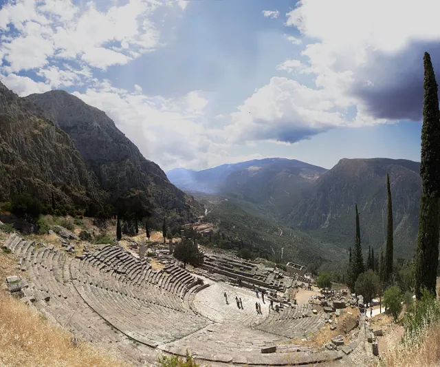 An ancient stone theatre on a slope, with a mountain ridge and valley behind it