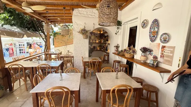 A whitewashed space with wicker lamps, marble tables, wooden chairs and decorative plates on the wall