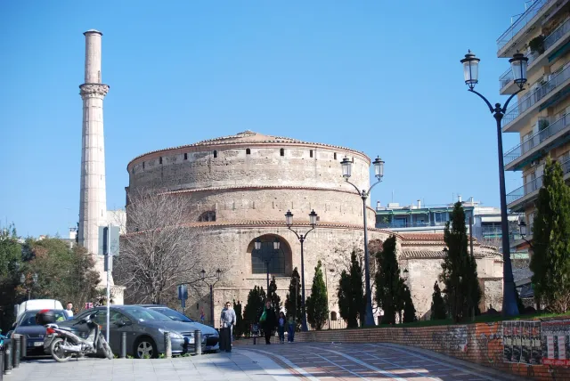 A massive round brick building with a minaret beside it, on a city square