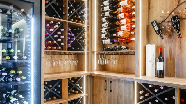 A wine cellar with wooden racks full of bottles and glasses hanging above