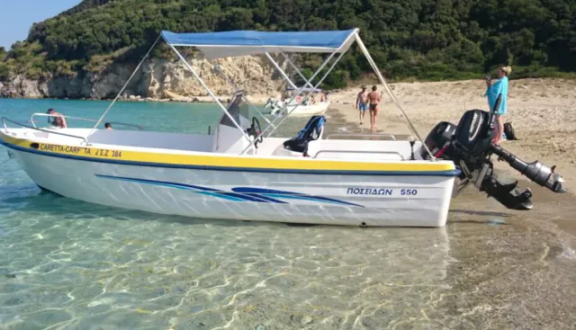 A small motorboat with a blue canopy in shallow water, and people on the sand