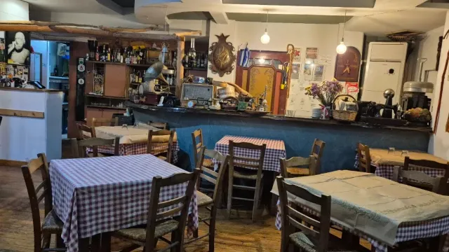 A rustic interior with a wooden counter full of objects, red checked tablecloths and wooden chairs