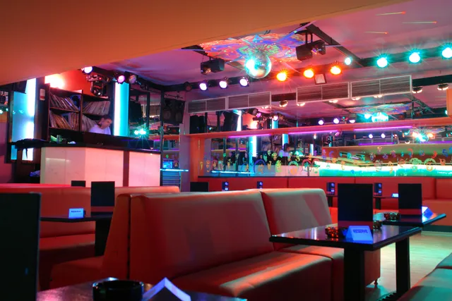 Red leather sofas facing a dance floor, with a disco ball and colourful lighting