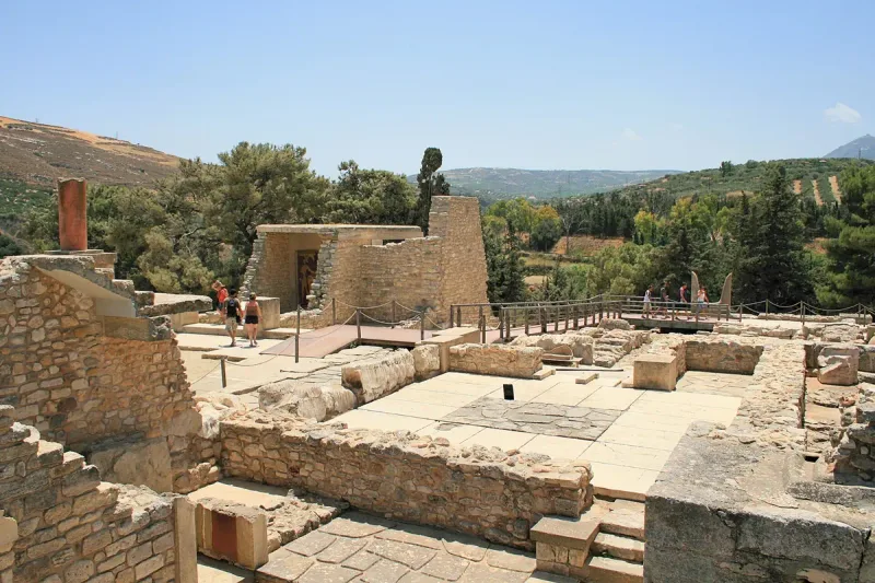 Excavations of an ancient palace with stone walls and steps, green hills behind