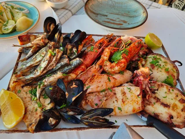 A wooden board loaded with grilled sardines, mussels, shrimp and squid with lemon
