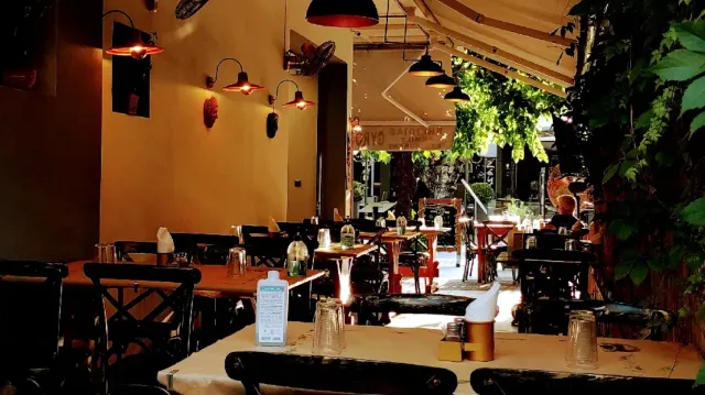 A covered space in the evening with an ochre wall, red lamps, wooden tables and climbing greenery