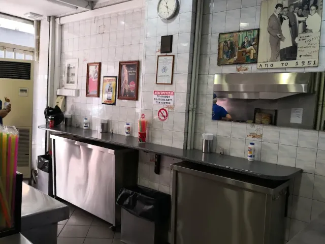 A kitchen tiled in white ceramic with stainless steel counters and framed old photographs