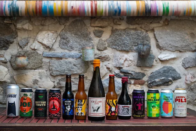 A row of beer cans and bottles with colourful labels, in front of a stone wall