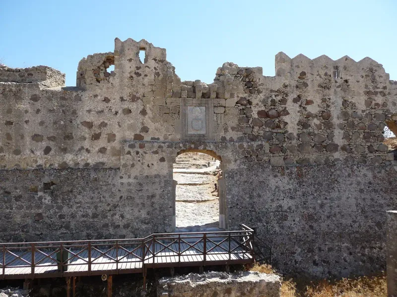 An arched gateway in the stone wall of Antimachia castle on Kos, with a small wooden bridge in front
