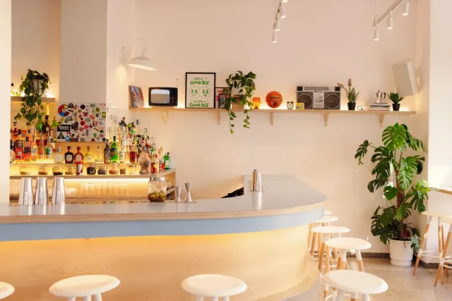 A light curved counter with stools, a bottle shelf, plants and an old radio