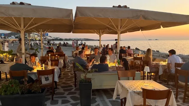A seafront terrace at sunset with large parasols, many diners and a pebble mosaic floor