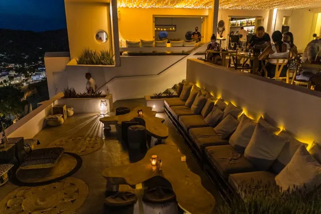 A night terrace with a long cushioned bench, low tables and warm lighting