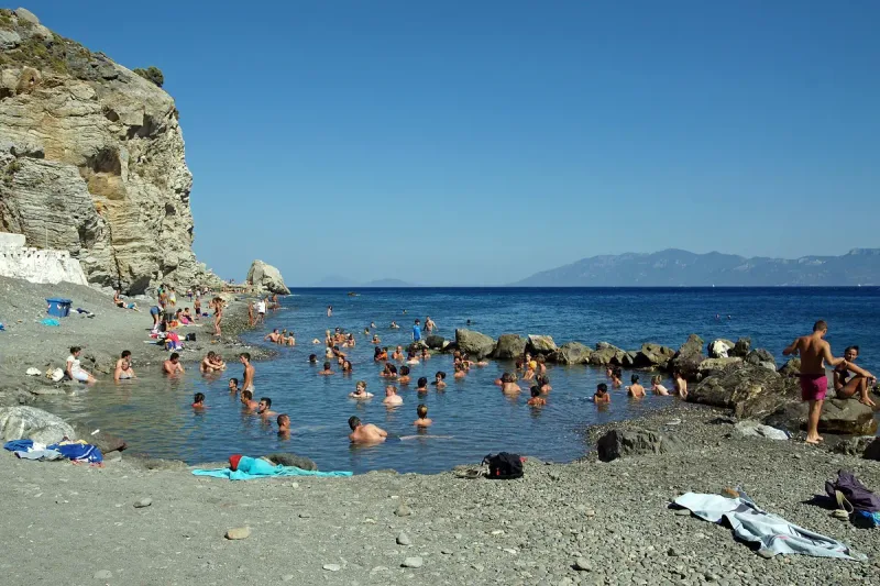 Bathers in a rock enclosed hot spring pool on the pebble beach of Therma in eastern Kos