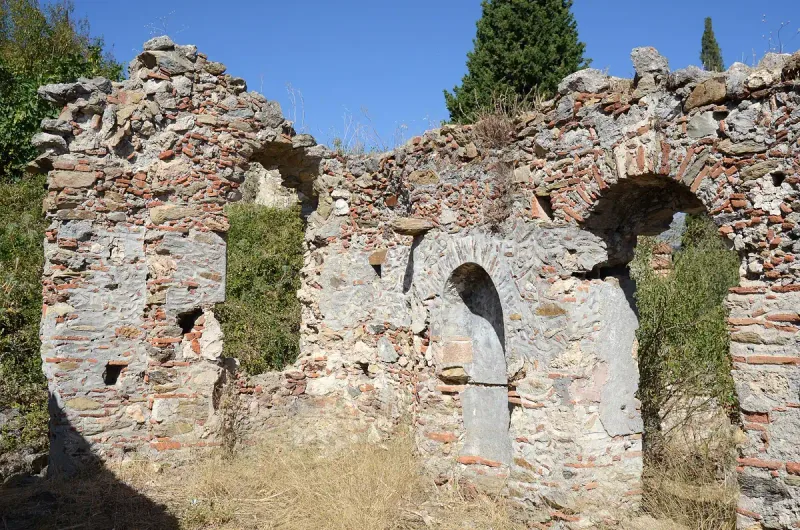 A ruined wall of stone and red brick with arched niches against a blue sky