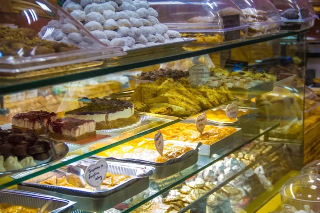 A glass display case with cakes, trays of syrupy pastries and powdered cookies