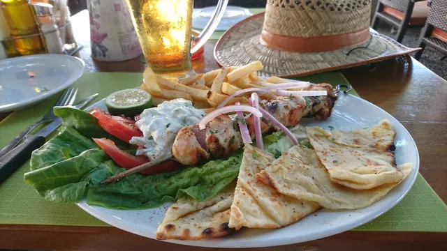 A plate of chicken skewer with pita, tzatziki, fries and salad, beside a glass of beer