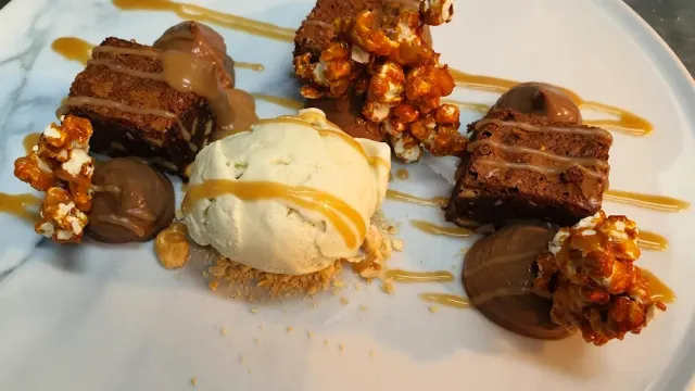 A dessert plate with a scoop of ice cream, cake pieces, caramel popcorn and chocolate smears