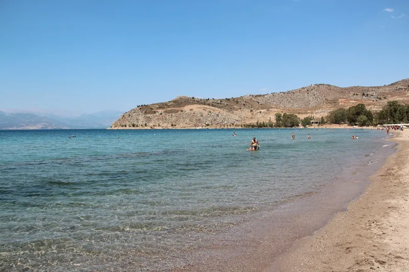 The curving bay of Karathona beach near Nafplio, with shallow water and swimmers