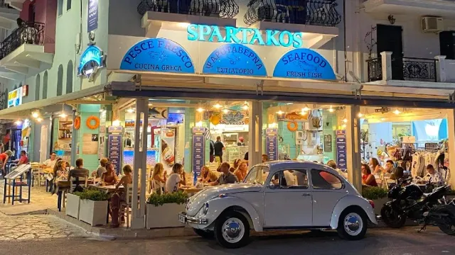 A frontage lit in the evening with full tables and a white beetle car parked in front