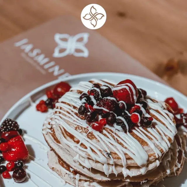 A stack of pancakes with white glaze and red and black berries on a plate