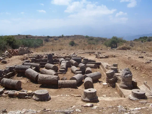 Vaulted stone remains of an ancient water cistern in an open field, with hills behind