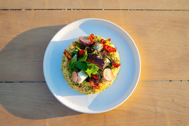 A colorful salad dish with radish and chili in a white plate on a wooden table