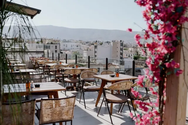 Wicker chairs and white tables on a rooftop, pink bougainvillea and the city roofs behind