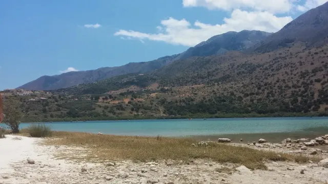 A green blue lake ringed by mountains, with a strip of sand in the foreground