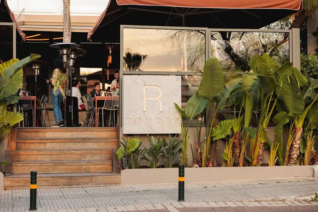 An entrance with wooden steps, tropical plants and a stone sign, with people seated on the terrace above