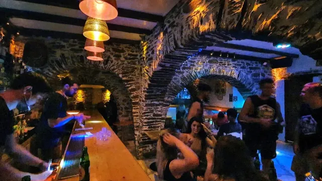 A long wooden counter and a dense crowd in a stone space, with hanging lamps at night