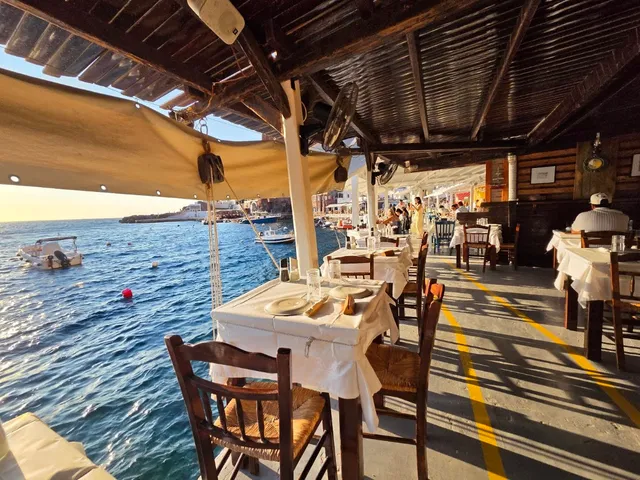Tables set with white tablecloths under a wooden awning, right by the water and moored boats