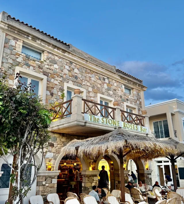 A stone building with a wooden balcony and a straw canopy over outdoor seating