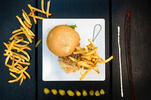 A burger with fries on a white plate, shot from above on a dark wooden table