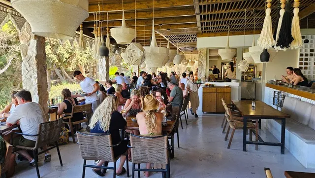 A busy covered terrace with woven light fixtures and long wooden tables