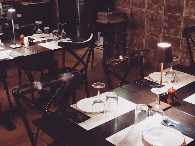 Dark wooden tables set with glasses and plates, with table lamps and a patterned tile wall