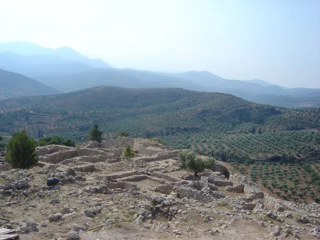 Stone foundations of an ancient city on a hilltop, with a valley and mountain ridges behind