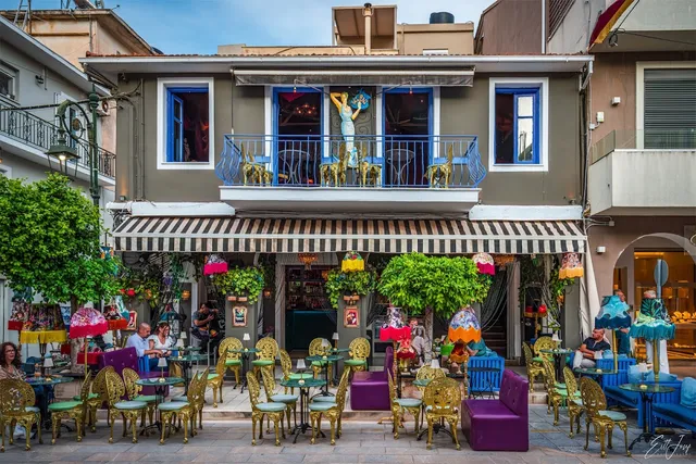 A colourful facade with a striped awning, gold chairs and purple sofas on the pavement