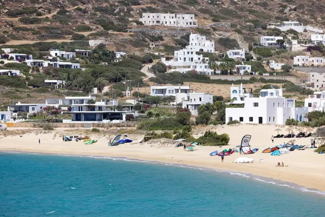 A wide sandy beach with clear blue water and white houses on the slope above