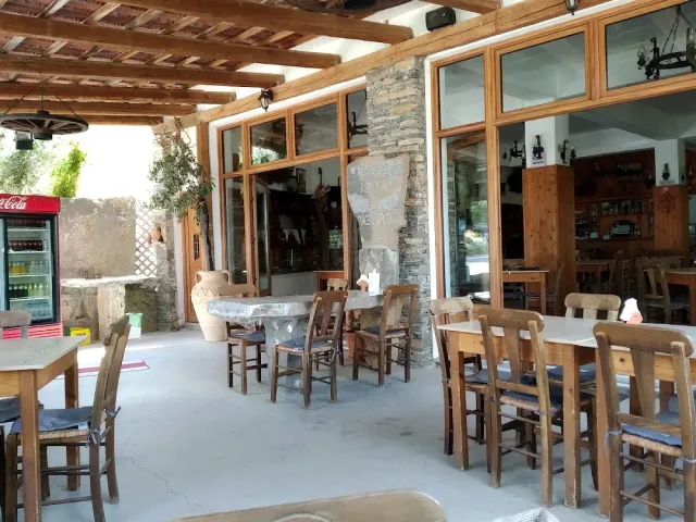 A veranda with a timber ceiling, wooden tables and chairs, a clay jar and a red drinks fridge