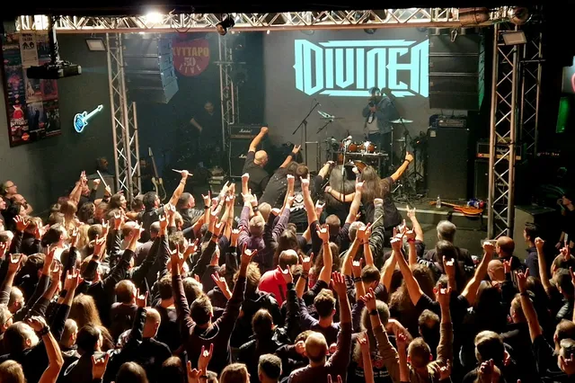 A packed crowd raises their hands before a band on a lit stage at a live show