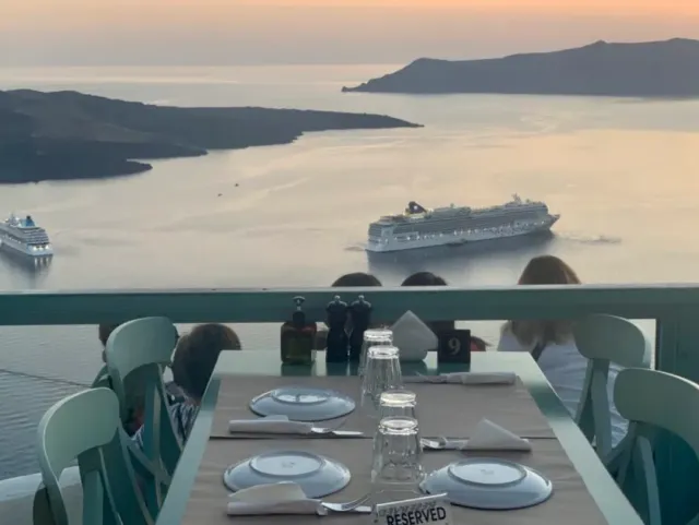 A laid table on a terrace facing a bay at sunset with two passenger ships