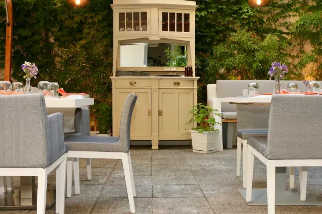 A courtyard with grey upholstered chairs, an old wooden cupboard and an ivy covered wall